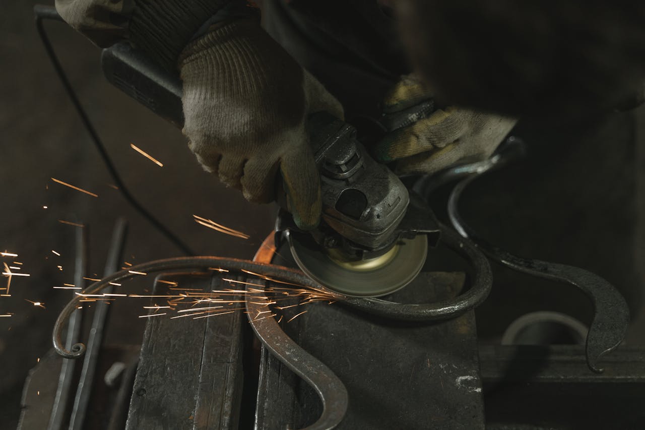 Metalworker using an angle grinder on metal with visible sparks in an industrial setting.